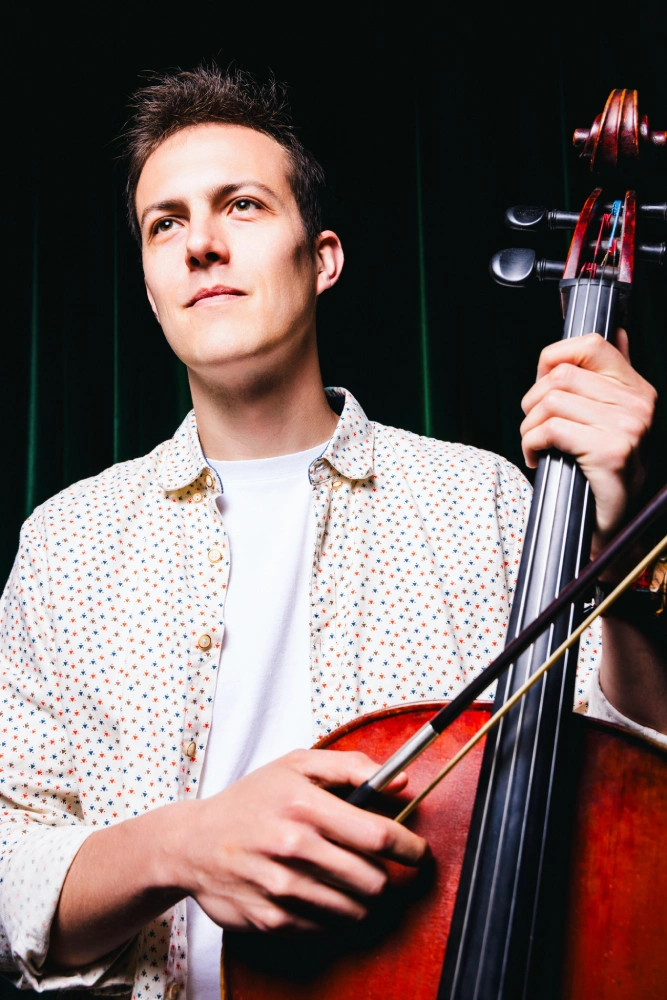 Simon Lannoy, violoncelliste, pose à la fin d'un concert avec son violoncelle devant un rideau noir sur scène pour les applaudissements